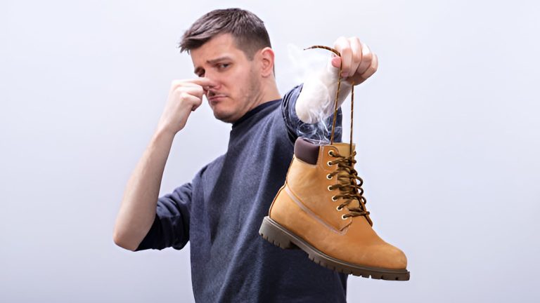 Close-up Of A Man Covering His Nose While Holding Stinky Shoe Against White Background